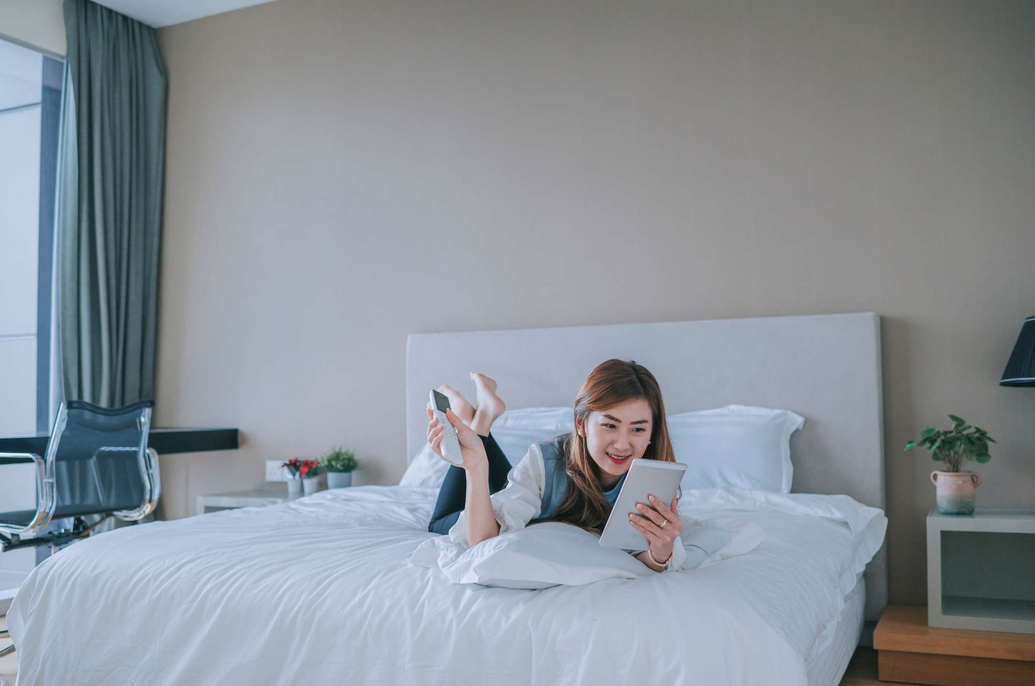 Woman reading with digital tablet lying down on bed while adjusting AC temperature