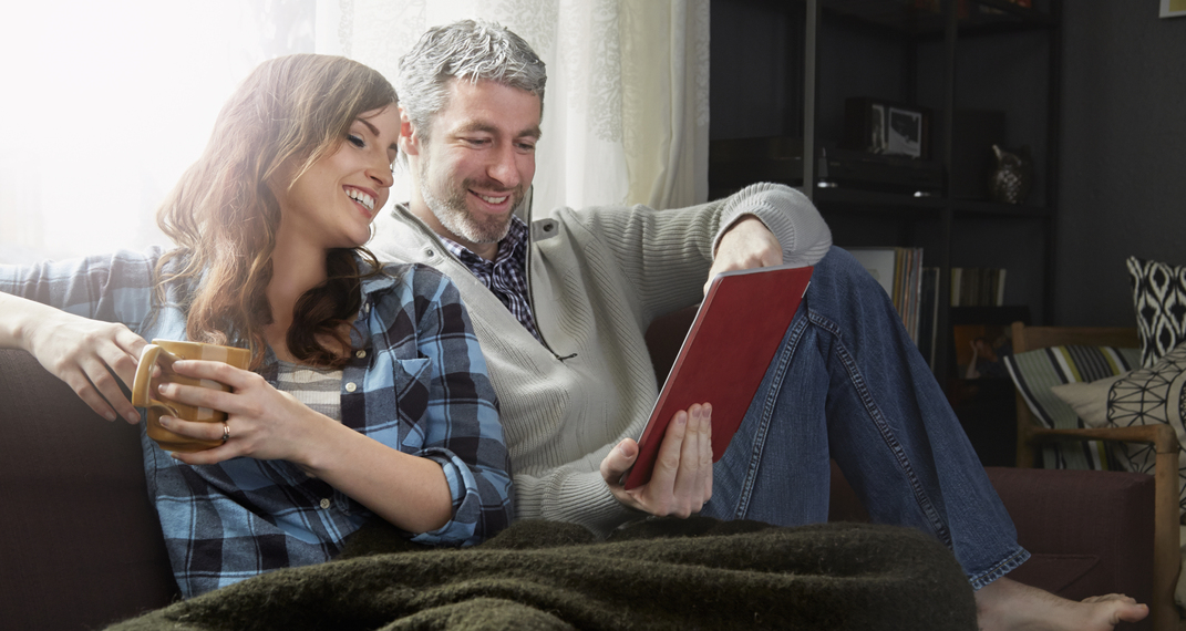 Couple sitting on sofa drinking coffee and looking at digital tablet