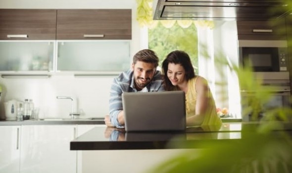 A man and a woman looking at a laptop in a kitchen